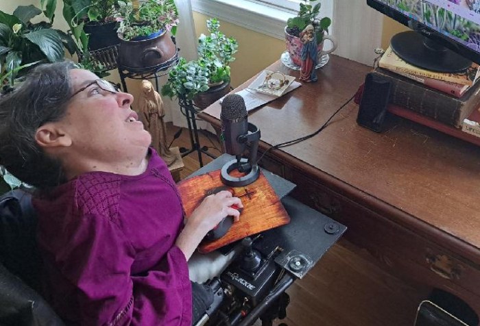 A woman, Christina Chase, sitting in a wheelchair at her computer