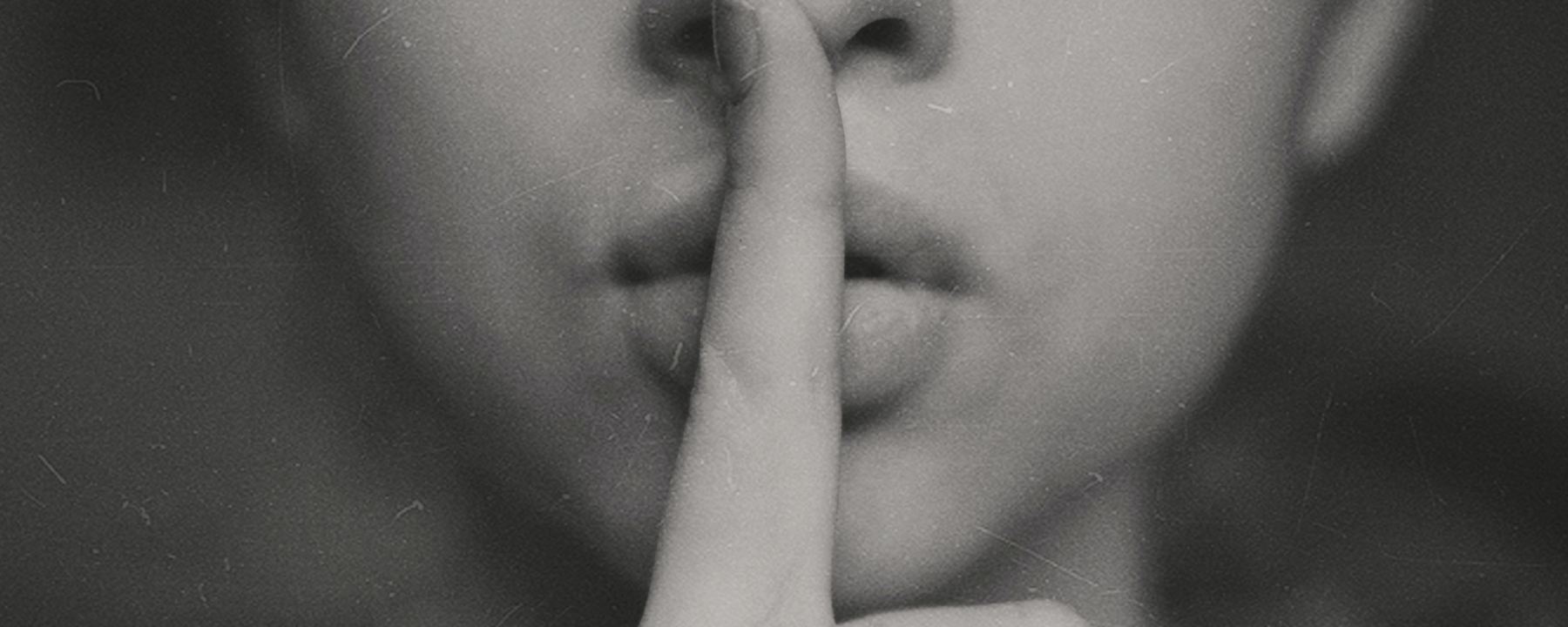 Close up of woman holding her finger against her lips in the sign of silence