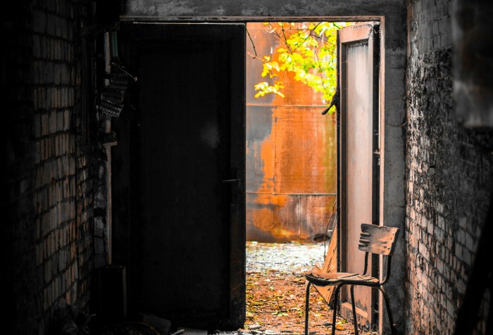A dark enclosed alley with an open door at the end showing golden light