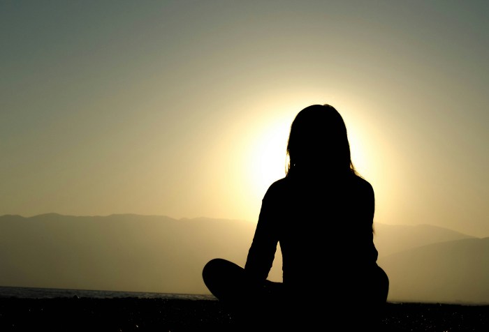 Silhouette of a woman sitting on the ground cross legged with the sun shining around her