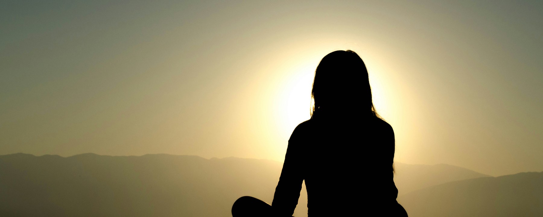 Silhouette of a woman sitting on the ground cross legged with the sun shining around her