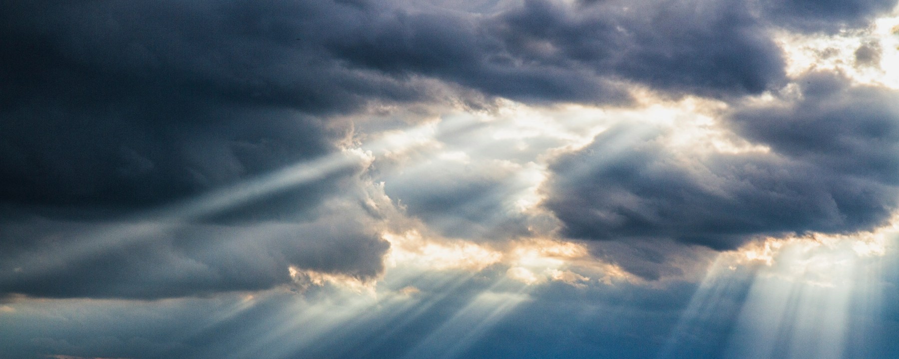 Rays of sun streaming through dark clouds onto a road that leads into the light