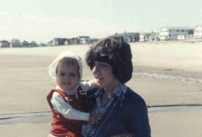Young mother holding a baby girl on a beach in the 1970s