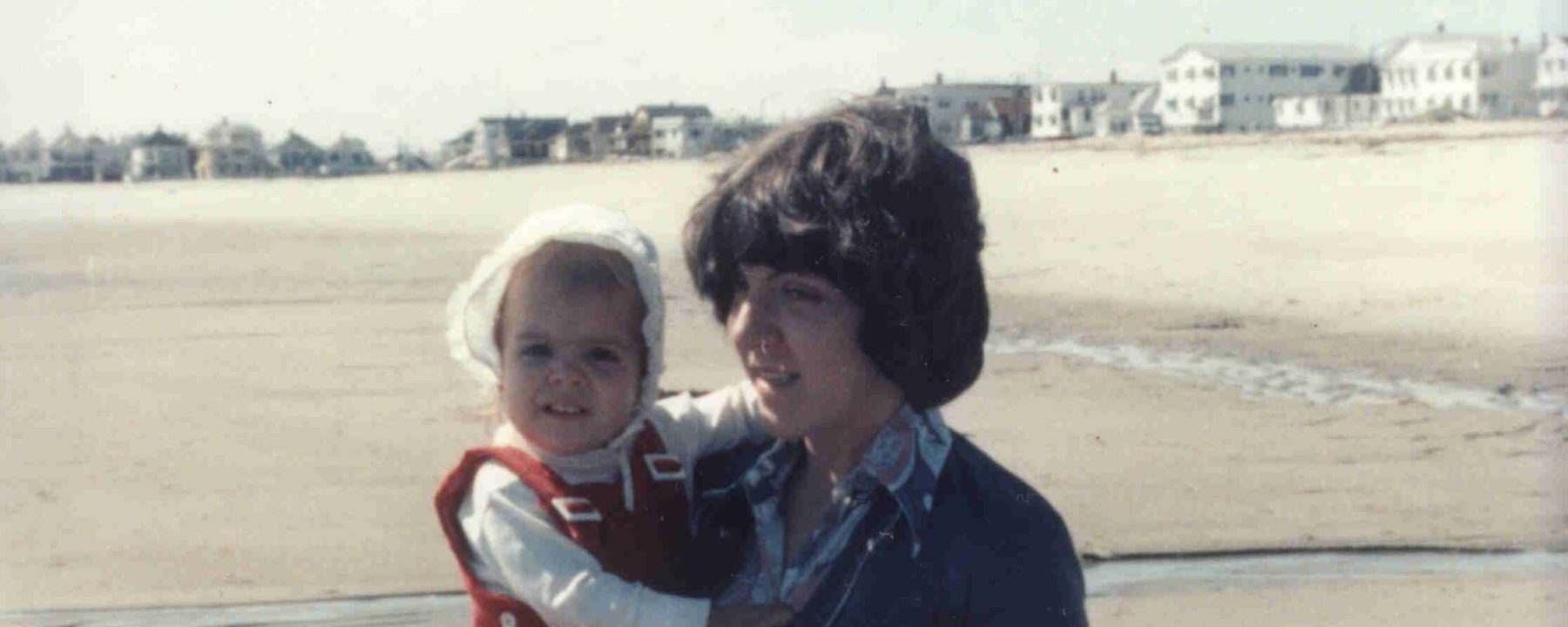 Young mother holding a baby girl on a beach in the 1970s